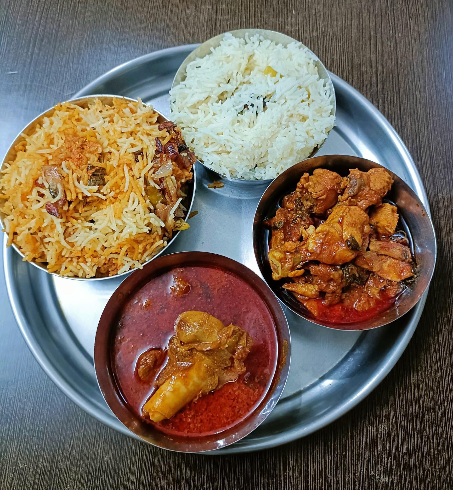 A steel thali with four compartments of biryani, rice, chicken and mutton curry