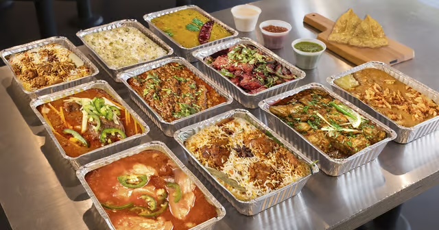A small catering spread packed in foil trays with rice, curries and chips