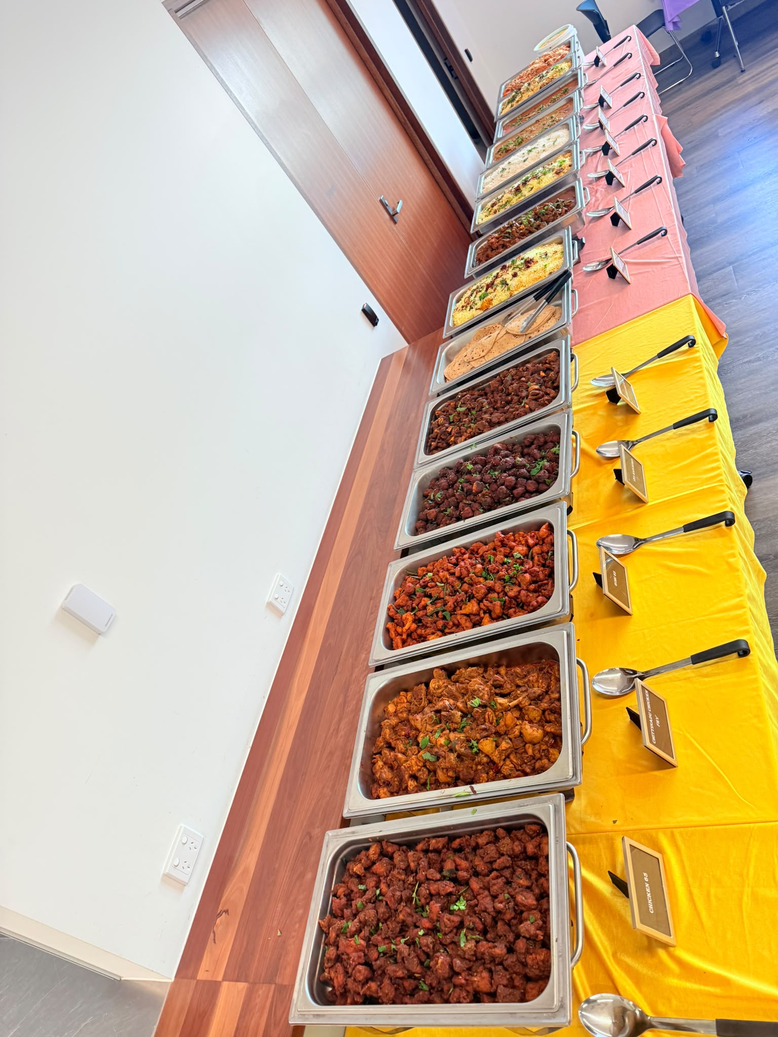 A long buffet table with multiple chafing dishes of curries, rice and paneer